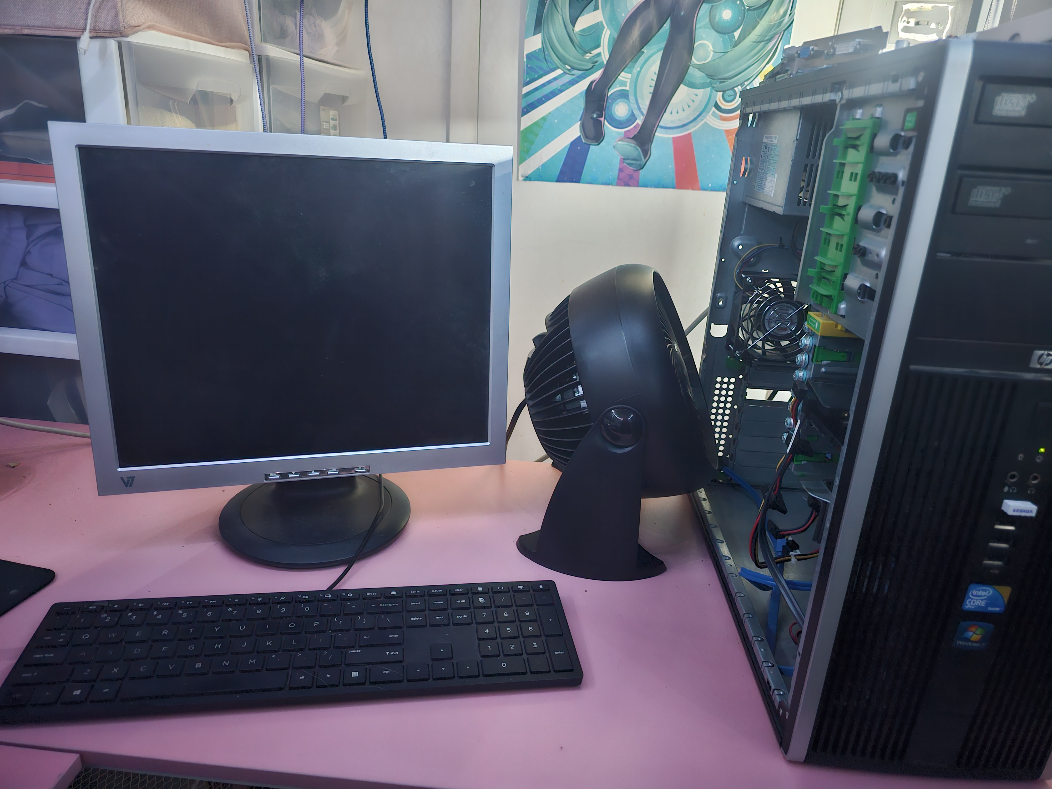 A square monitor next to an open PC with a fan pointing into it on a pink desk
